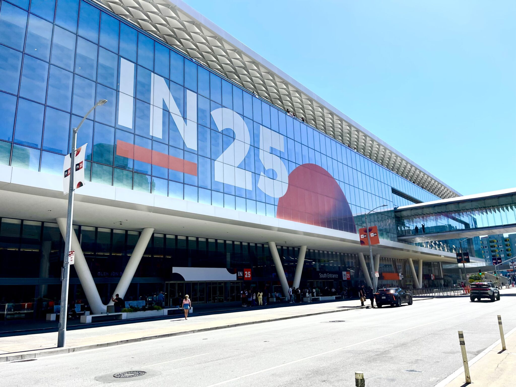 A glass convention center with a large IN25 banner across its facade under a clear blue sky
