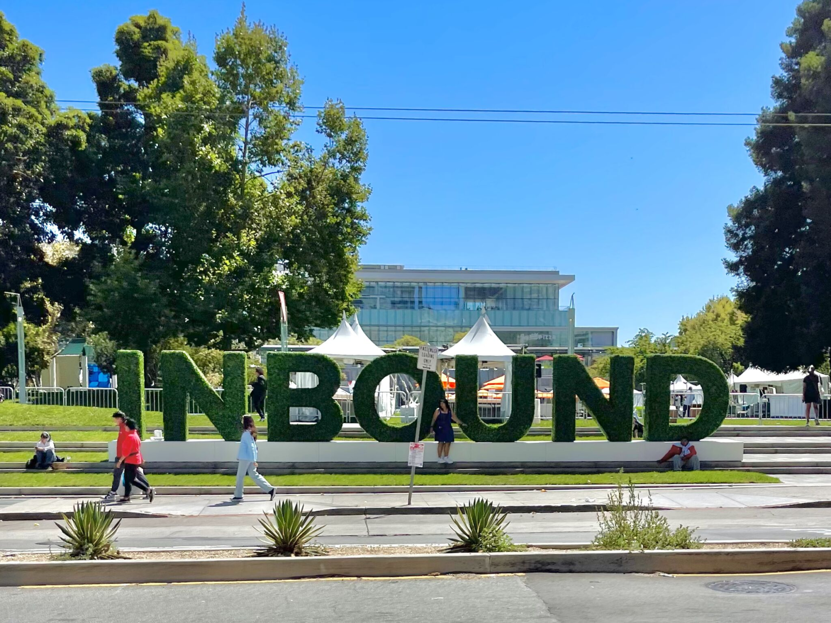 Giant hedge letters spelling INBOUND on a lawn beside a city street