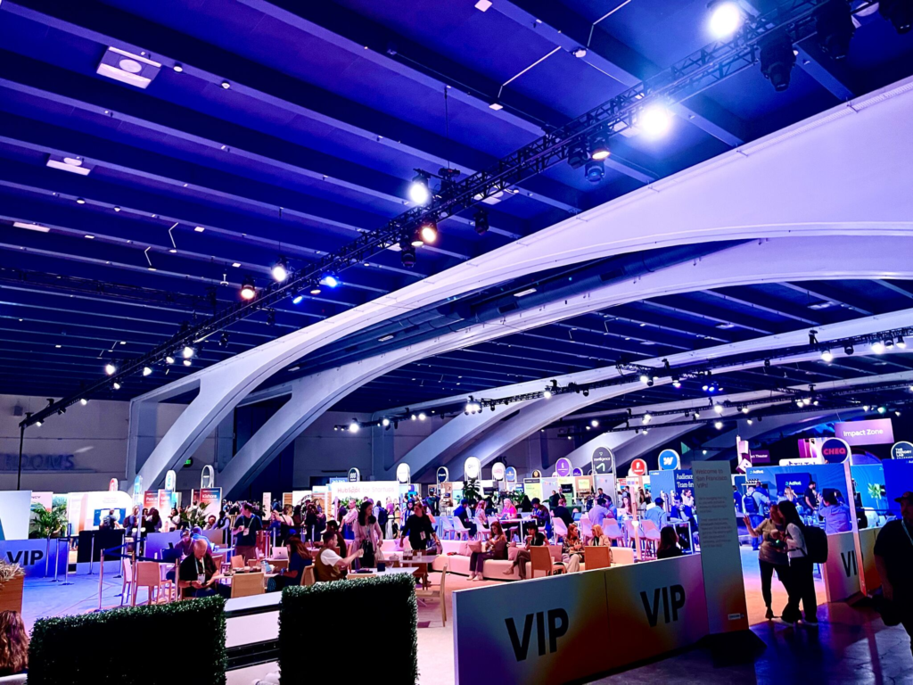 An expo hall lit in blue and purple, with lounge seating and VIP signs