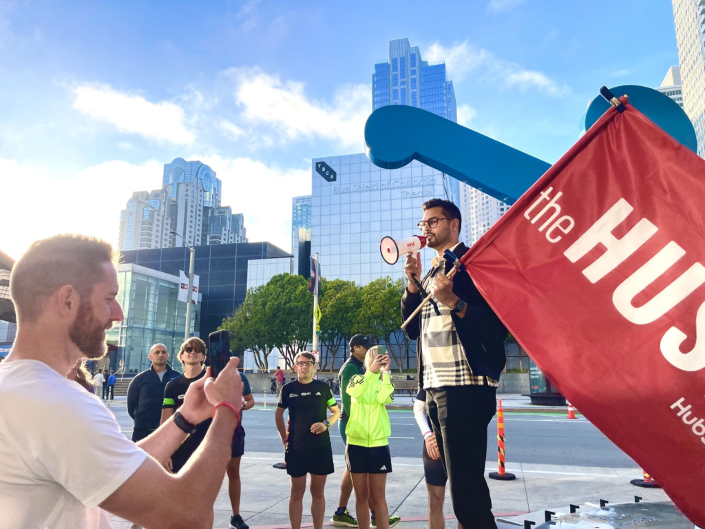 A speaker with a megaphone leads a morning run group beside a red event flag