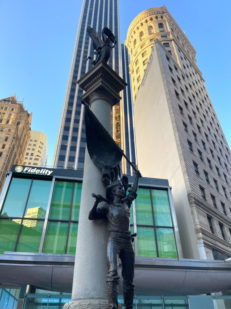 A bronze statue on a tall column, framed by high-rise towers