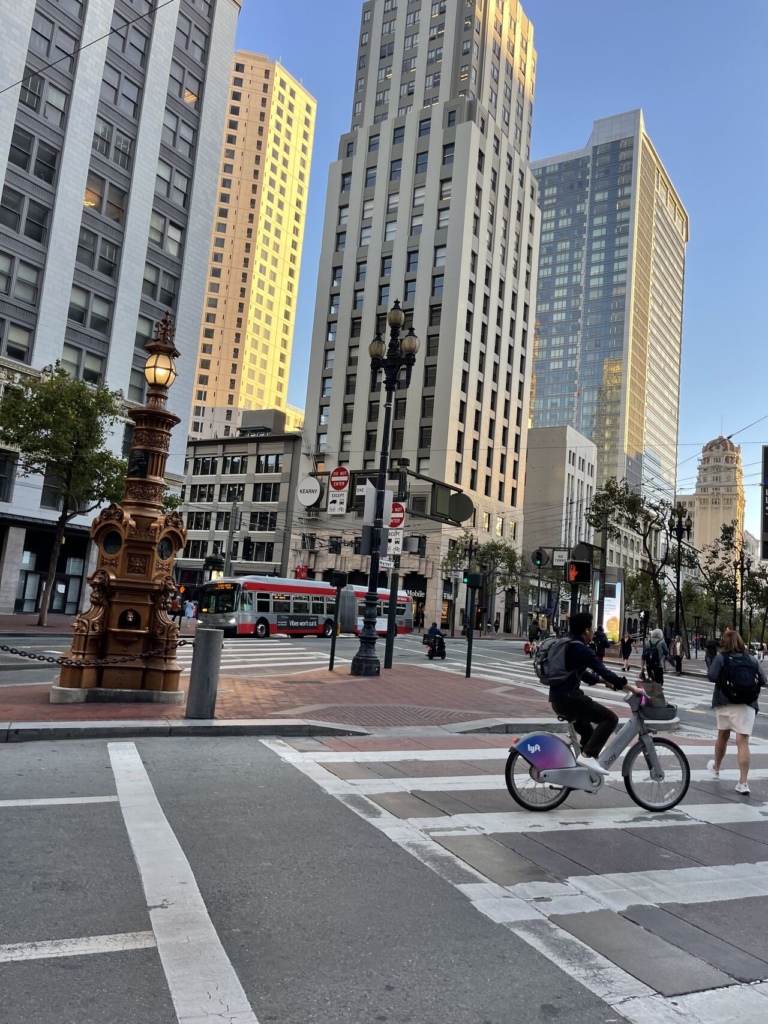 A downtown intersection with a cyclist, an ornate column and tall office buildings