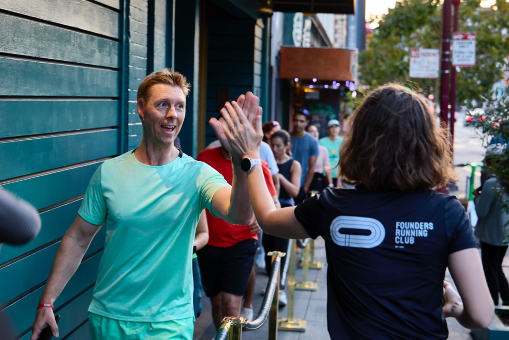 Two runners high-five on a sidewalk; one wears a Founders Running Club shirt