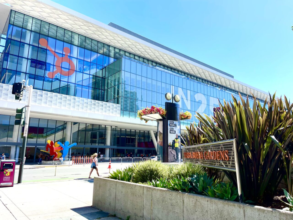 A glass convention center with an IN25 banner and landscaped planters out front